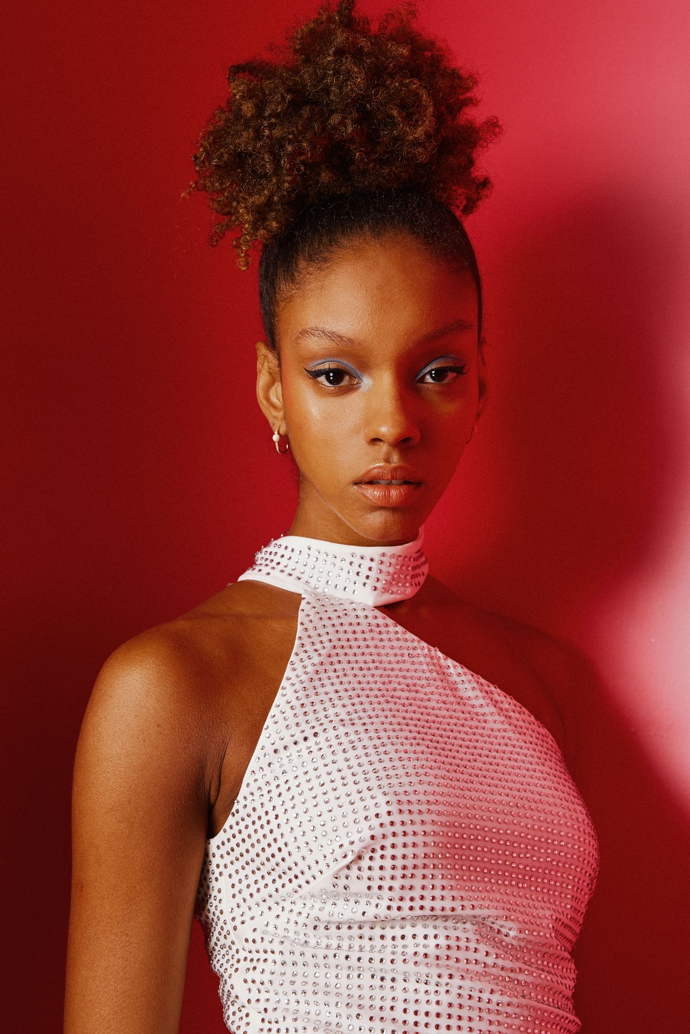 A crystal-studded white halter catches the red glow in a tight beauty portrait for Alia Studio.