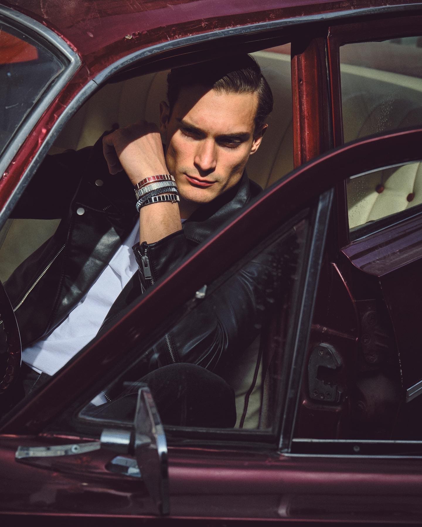 Sunlit stacks of Dime Tribe bracelets frame the model's face as he leans from the door of a burgundy classic car.