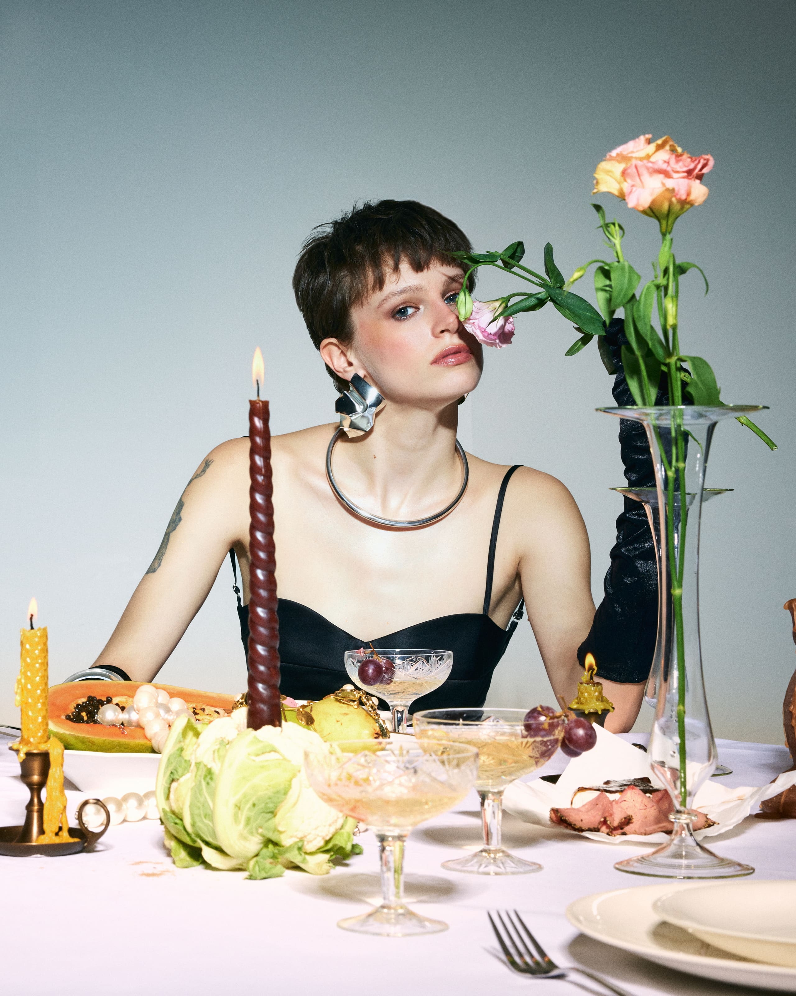 A pixie-cropped gaze through lisianthus blooms, the black Mers Silk bustier framed by a sculpted silver collar.